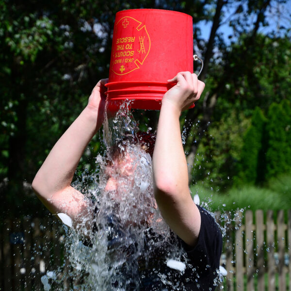 Eine Person schüttet sich einen roten Eimer mit Wasser und Eis über den Kopf im Freien.