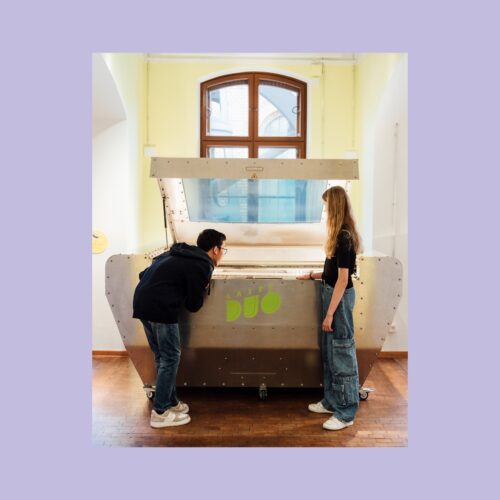 Zwei Personen betrachten eine große, metallische Maschine mit der Aufschrift "Laser Duo" in einem Raum mit großen Fenstern.