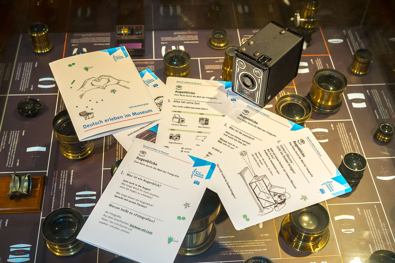 Lern-Material "Deutsch erleben im Museum" mit Aufgabenblättern zu Fotografie und historischen Kameras auf einem Ausstellungstisch.