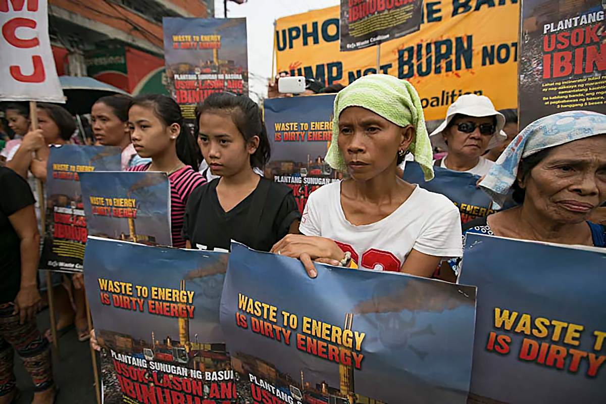 Gruppe von Demonstrantinnen hält Plakate mit Aufschriften wie "Waste to Energy is Dirty Energy" und protestiert gegen Müllverbrennungsanlagen auf der Straße.