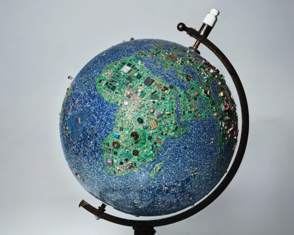 Globus aus unzähligen elektronischen Bauteilen und Platinen, die die Kontinente bilden, auf schwarzem Ständer vor hellem Hintergrund.