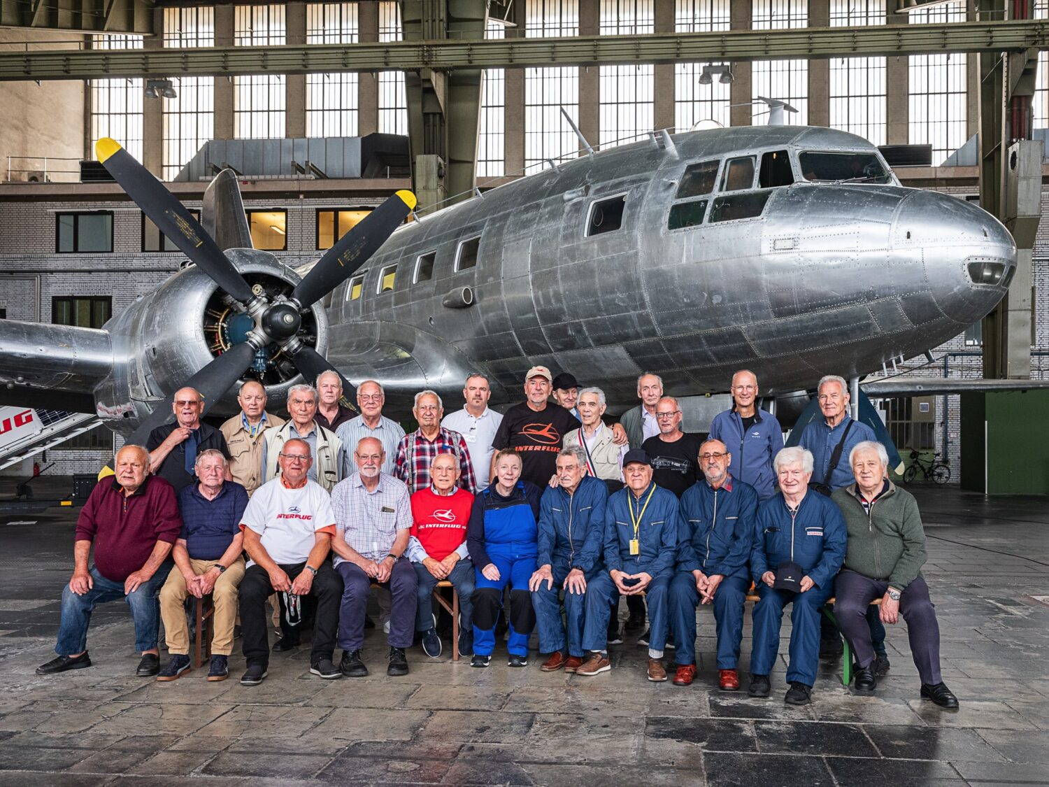 Gruppenfoto der Ehrenamtlichen vor einem historischen Propellerflugzeug in einer Halle, einige tragen Arbeitskleidung.