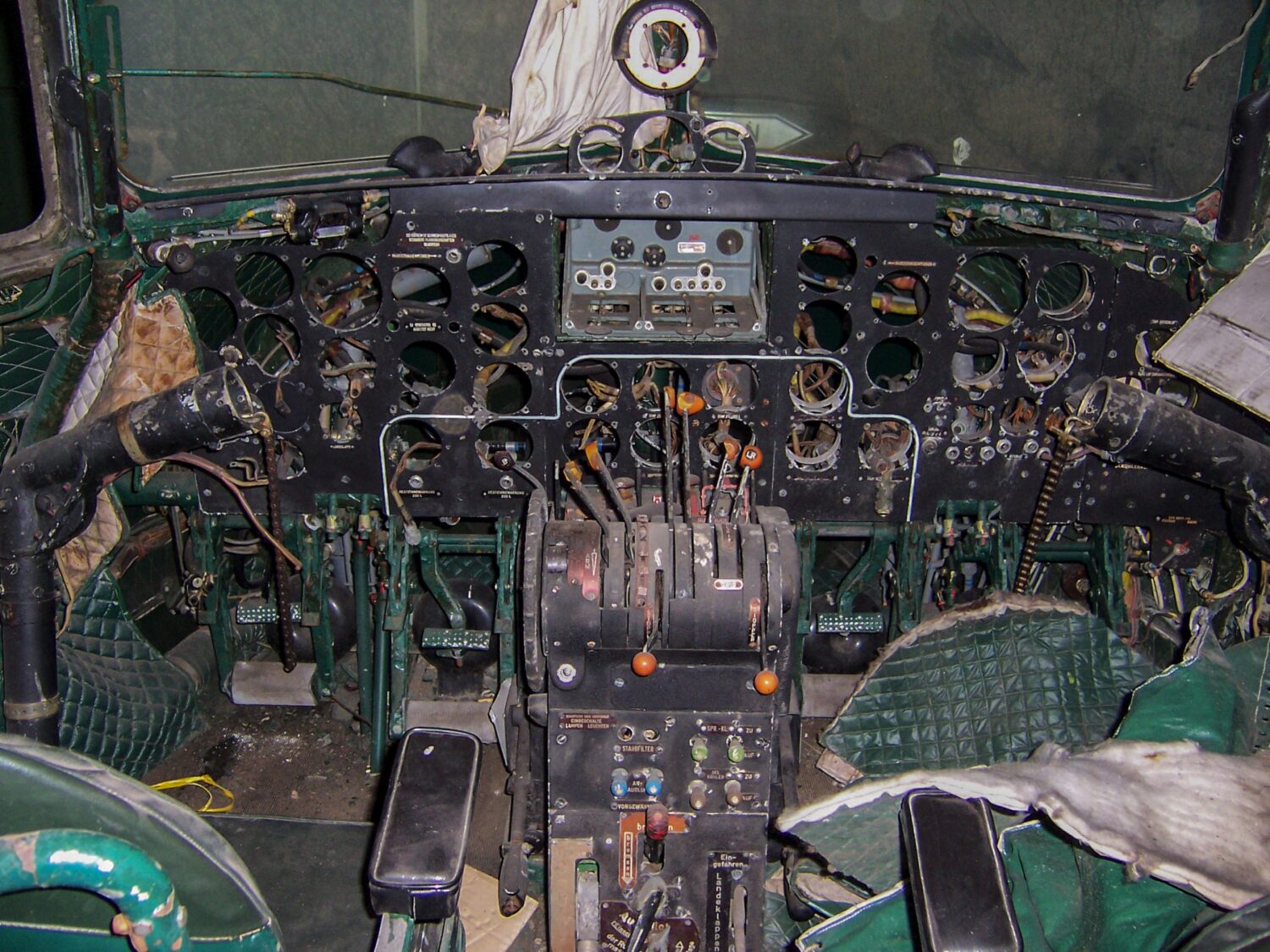 Historisches Flugzeugcockpit mit analoger Instrumentenkonsole, Steuerknüppeln, Schaltern und grüner Polsterung in schlechtem Zustand.