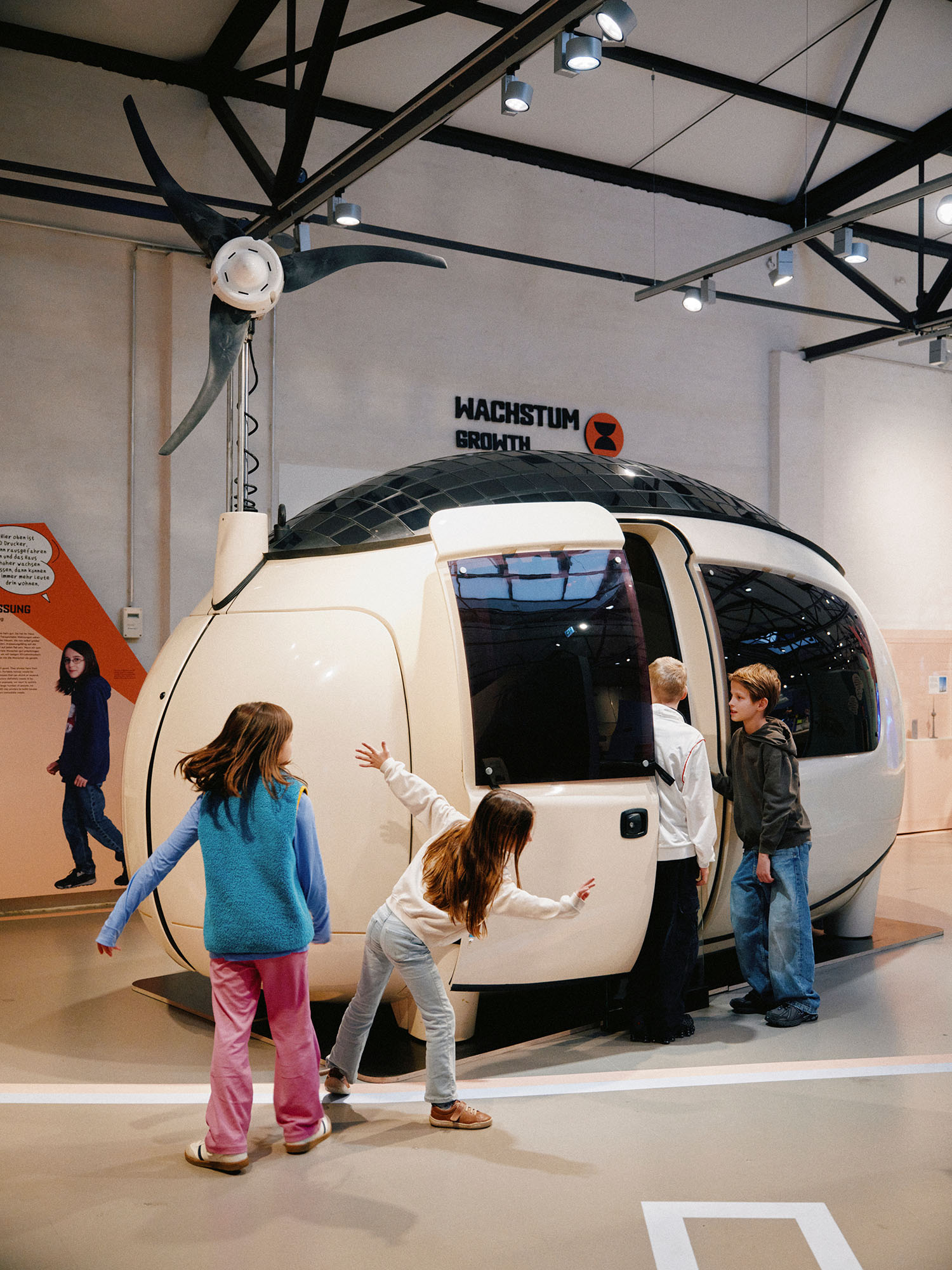 Kinder erkunden eine futuristische, eiförmige Wohnkapsel in einer Ausstellung.