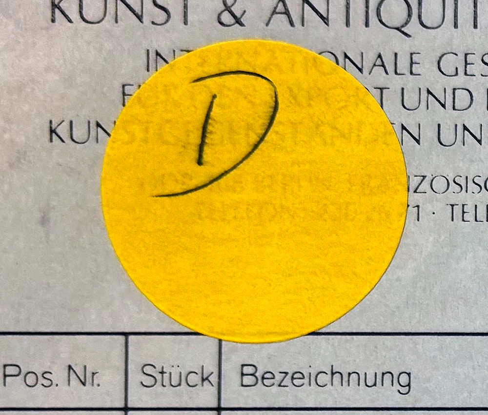 Gelber runder Aufkleber mit handschriftlichem ‚D‘ auf einer Tabelle mit Spalten für Pos. Nr., Stück und Bezeichnung.