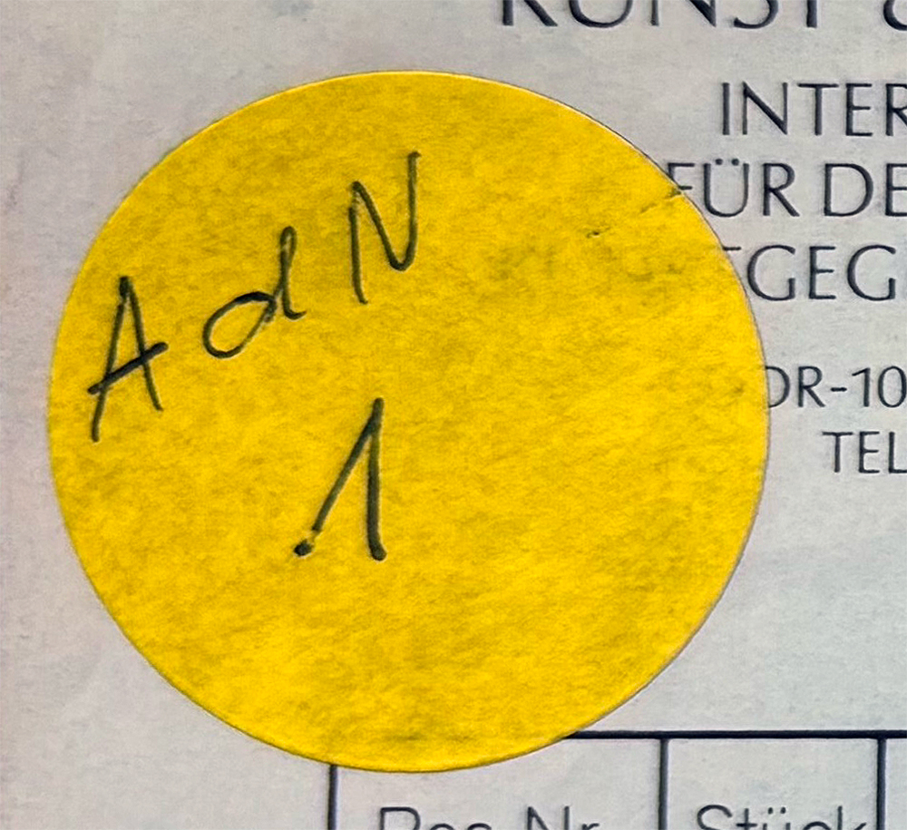Nahaufnahme eines gelben, runden Aufklebers mit der handschriftlichen Aufschrift „AlN“ auf einem gedruckten Dokument.