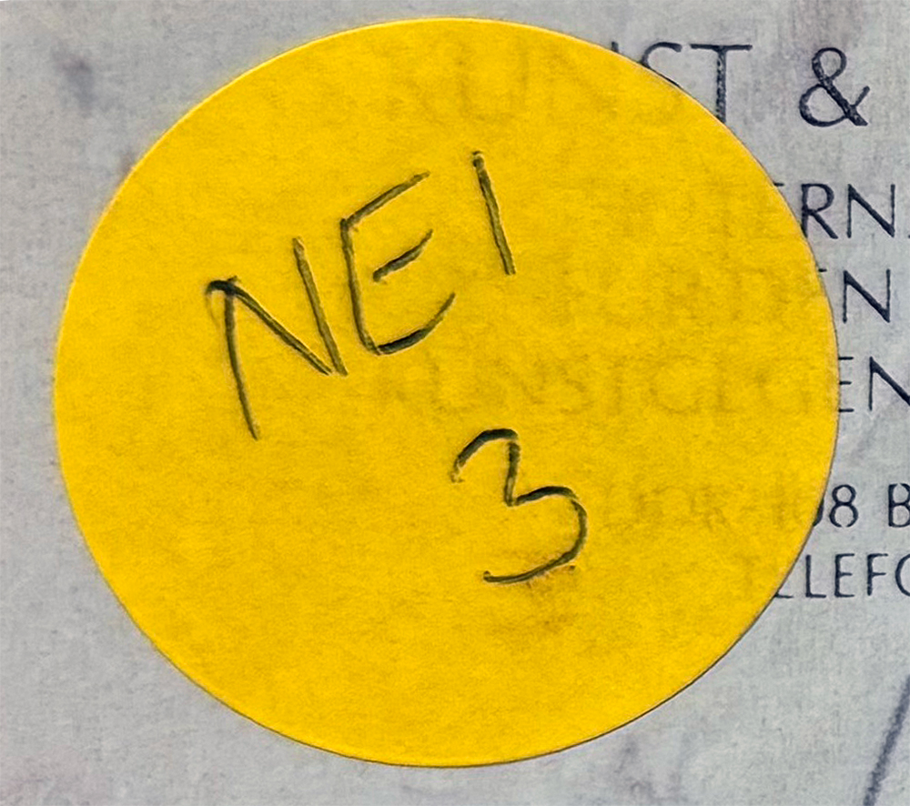 Nahaufnahme eines gelben, runden Aufklebers mit der handschriftlichen Aufschrift „NEI“ und einer darunter stehenden handschriftlichen „3“ auf einem gedruckten Dokument.