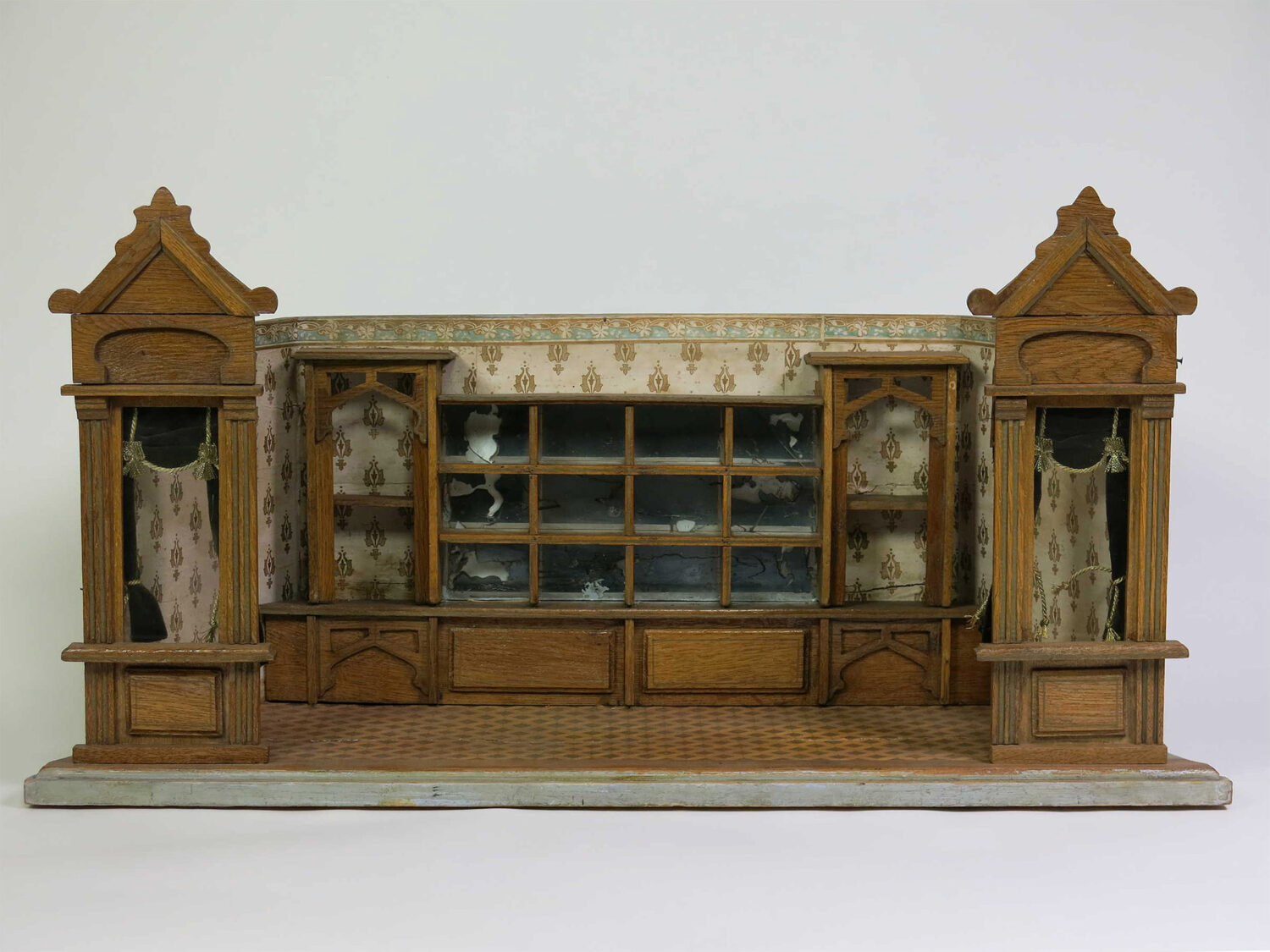 Historisches Puppenstubenmöbel aus Holz mit zwei Türmen, verglastem Schrank, Schubladen und gemusterten Tapeten.