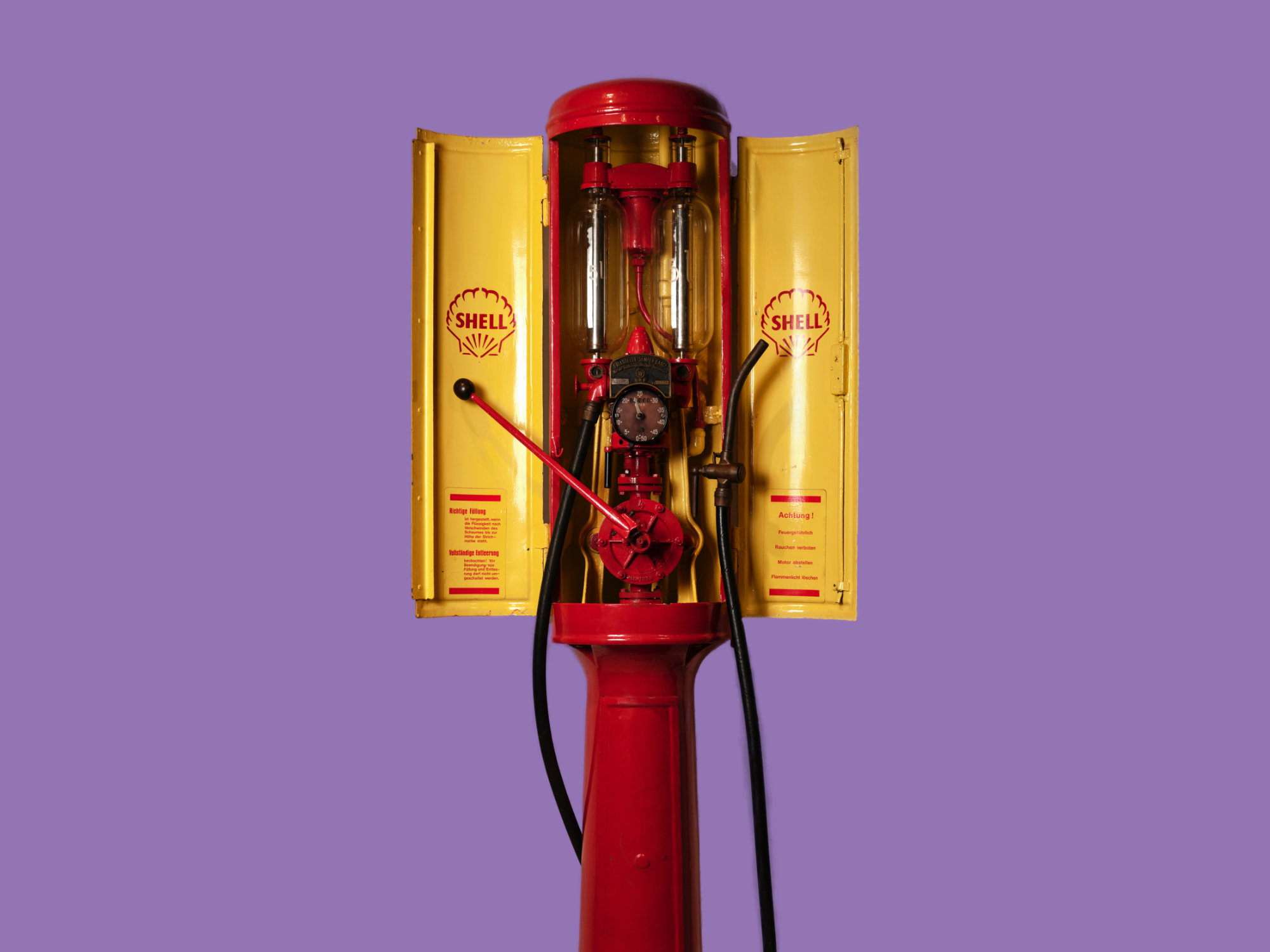 Historische rote und gelbe Shell-Benzinzapfsäule mit sichtbarer Mechanik, Schläuchen und Messanzeige vor violettem Hintergrund.